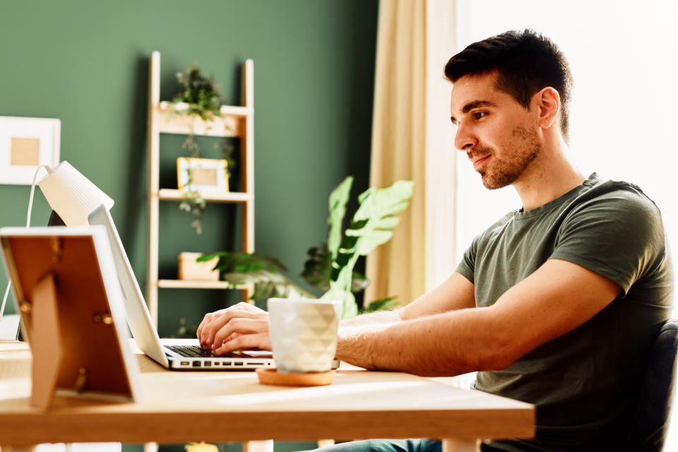 Young man sits at a desk at home and using laptop