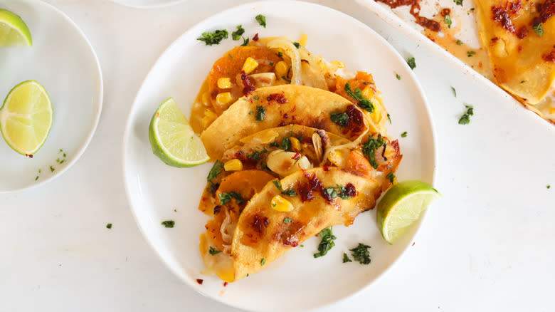 squash and corn quesadilla with limes on white plate