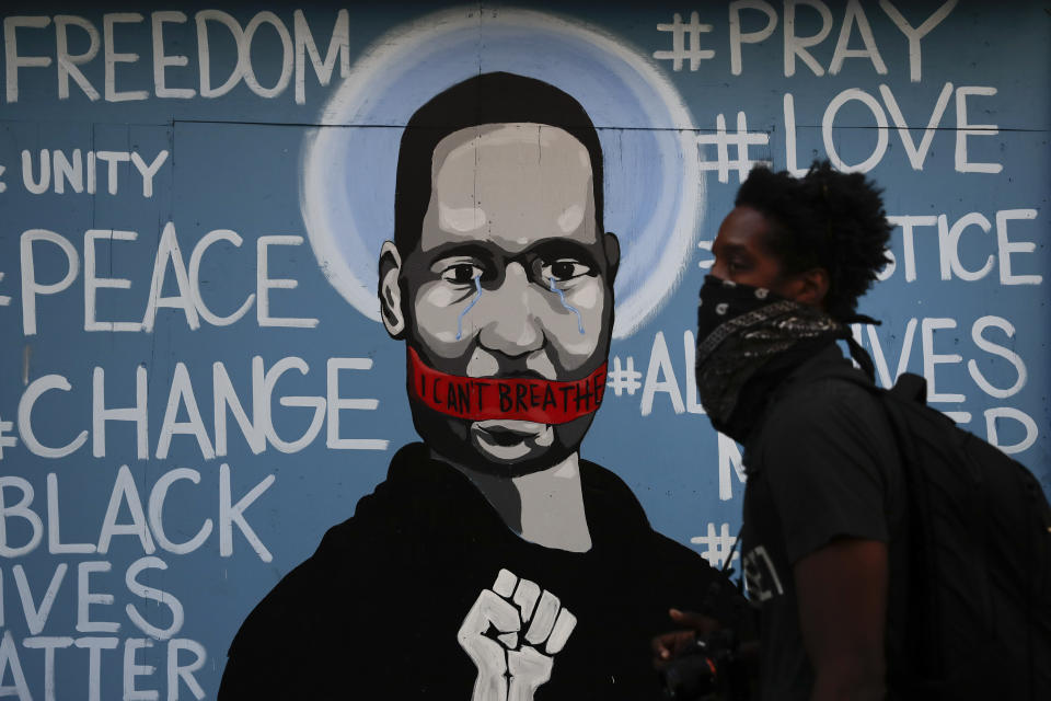 A man with a face covering walks past a mural depicting George Floyd during a protest over the death of Floyd Sunday, May 31, 2020, in Los Angeles. Floyd died in Minneapolis on May 25 after he was pinned at the neck by a police officer. (AP Photo/Jae C. Hong)