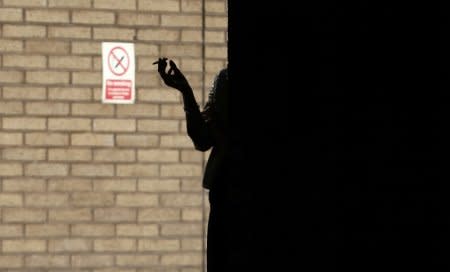 FILE PHOTO: A woman smokes in the shadows outside Southwark Crown Court in central London, March 5, 2014. REUTERS/Andrew Winning