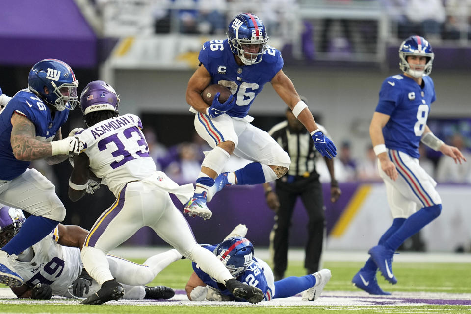 New York Giants running back Saquon Barkley (26) leaps over the line of scrimmage ahead of Minnesota Vikings linebacker Brian Asamoah II (33) during the first half of an NFL football game, Saturday, Dec. 24, 2022, in Minneapolis. (AP Photo/Abbie Parr)