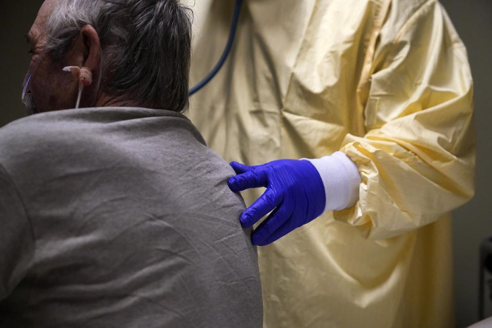 FILE - In this Nov. 24, 2020, file photo, Dr. Shane Wilson, right, touches the back of COVID-19 patient Glen Cowell while listening to Cowell's lungs through a stethoscope at Scotland County Hospital in Memphis, Mo. After a punishing fall that left hospital struggling, some Midwestern states are seeing a decline in new coronavirus cases. But the signs of improvement are offset by the infection's accelerating spread on both coasts. (AP Photo/Jeff Roberson, File)