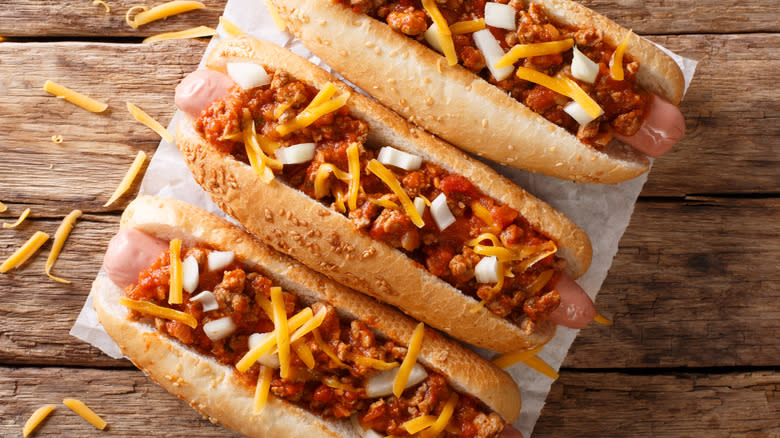 3 Chili dogs with cheese on a wooden board