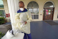 Dr. Robin Armstrong puts on his gloves while demonstrating his full personal protective equipment outside the entrance to The Resort at Texas City nursing home, where he is the medical director, Tuesday, April 7, 2020, in Texas City, Texas. Armstrong is treating nearly 30 residents of the nursing home with the anti-malaria drug hydroxychloroquine, which is unproven against COVID-19 even as President Donald Trump heavily promotes it as a possible treatment. Armstrong said Trump's championing of the drug is giving doctors more access to try it on coronavirus patients. More than 80 residents and workers have tested positive for coronavirus at the nursing home. (AP Photo/David J. Phillip)