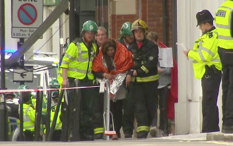  woman with blankets wrapped around her is being escorted by emergency services - Credit: Sky/AP