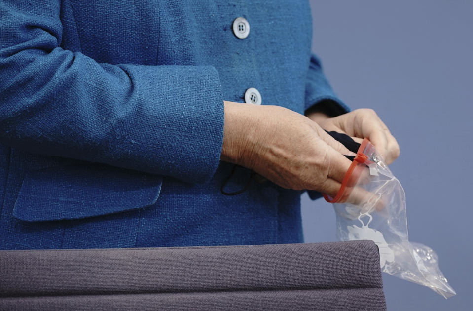 At the Federal Press Conference, Chancellor Angela Merkel puts her mask in a bag in front of her traditional summer press conference on current domestic and foreign policy issues. (Michael Kappeler/Pool via AP)