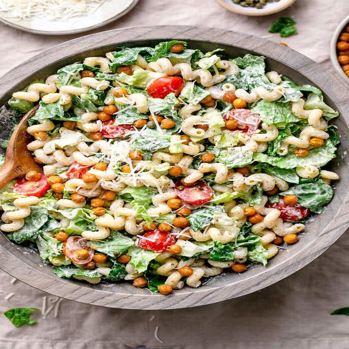 a bowl of salad with chickpeas, tomatoes, cheese, and spiral macaroni noodles