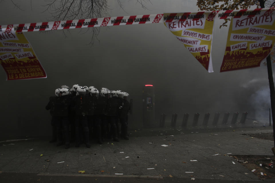 Riot police officers gather behind posters reading "pension" during a demonstration in Paris, Thursday, Dec. 5, 2019. Small groups of protesters are smashing store windows, setting fires and hurling flares in eastern Paris amid mass strikes over the government's retirement reform. (AP Photo/Rafael Yaghobzadeh)