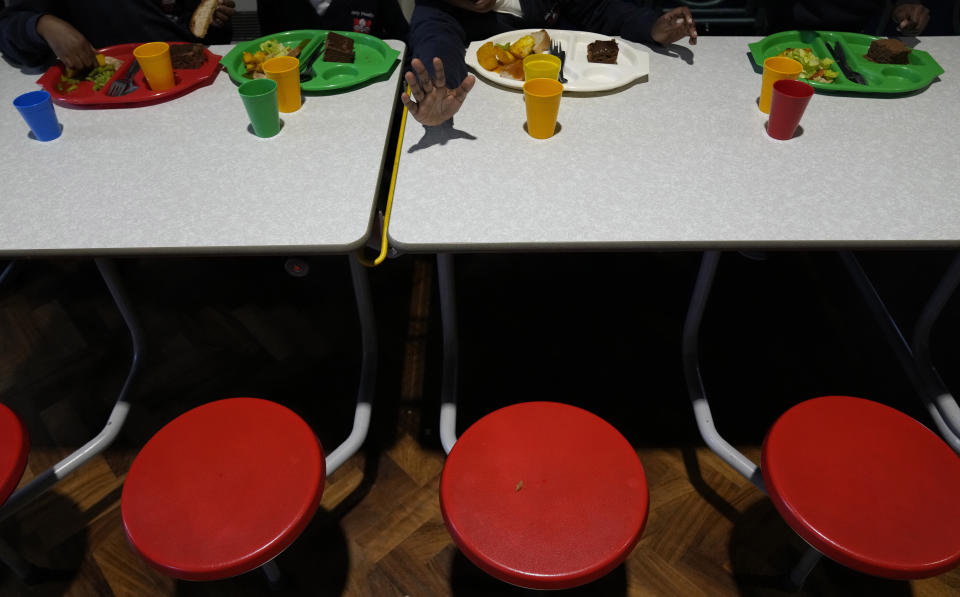 A pupil waves at the photographer as the children eat their lunch in the main hall of the Holy Family Catholic Primary School in Greenwich, London, Wednesday, May 19, 2021. Holy Family, like schools across Britain, is racing to offset the disruption caused by COVID-19, which has hit kids from low-income and ethnic minority families hardest. (AP Photo/Alastair Grant)