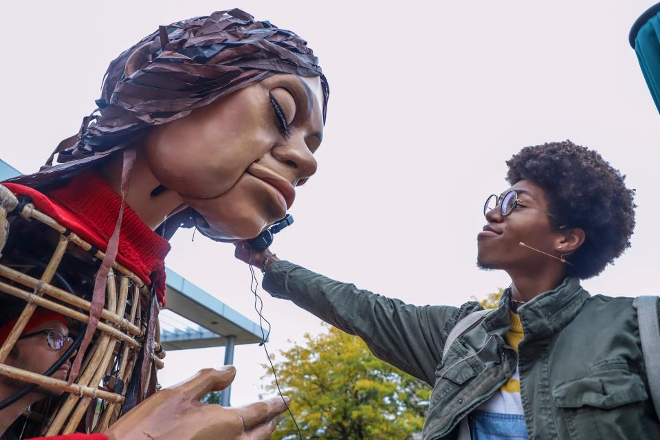 Daria Nimbee, 26, of Detroit, holds headphones playing music for Little Amal to listen to during a free public art display in southwest Detroit on Wednesday, Sept. 27, 2023. Amal is a 12-foot-tall puppet of a 10-year-old Syrian refugee girl who is traveling the globe to support displaced people everywhere and is a symbol of human rights. The Amal Fund with Choose Love supports displaced children across the world and accepts donations at chooselove.org/theamalfund