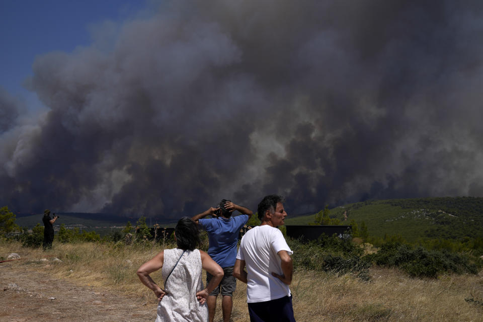 Residents watch as a wildfire burns on a hill in Pournari village near Athens, on Tuesday, July 18, 2023. In Greece, where a second heatwave is expected to hit Thursday, three large wildfires burned outside Athens for a second day. Thousands of people evacuated from coastal areas south of the capital returned to their homes Tuesday when a fire finally receded after they spent the night on beaches, hotels and public facilities. (AP Photo/Thanassis Stavrakis)