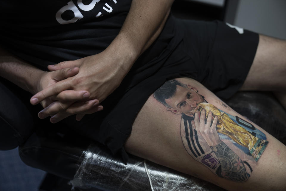 Sebastian Fernandez rests as artist César "Yeyo" Molina tattoos his leg with an image of soccer player Lionel Messi kissing the World Cup trophy, in Buenos Aires, Argentina, Thursday, Dec. 29, 2022. (AP Photo/Victor R. Caivano)
