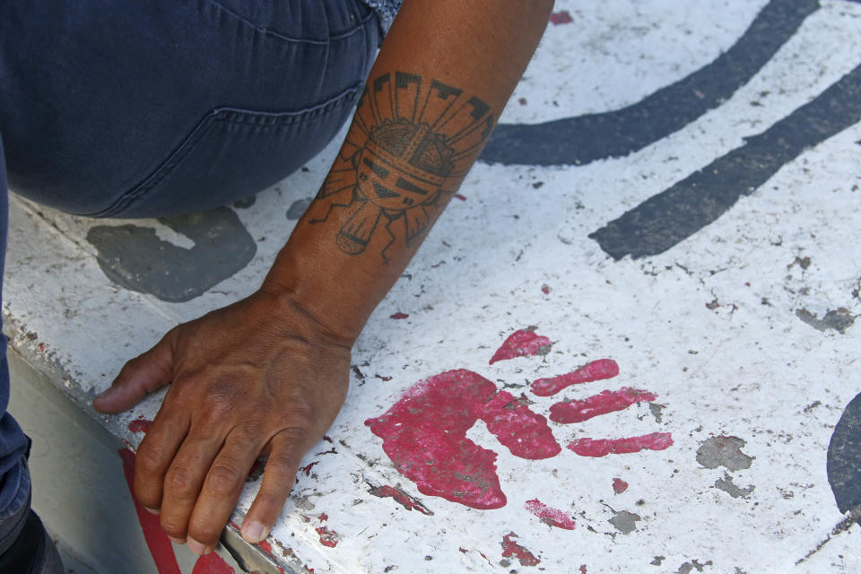 Native American advocate Carl Moore sits next to red handprint painted along a walkway which leads from the Bountiful High School parking lot up to the football field Tuesday, July 28, 2020, in Bountiful, Utah. While advocates have made strides in getting Native American symbols and names changed in sports, they say there's still work to do mainly at the high school level, where mascots like Braves, Indians, Warriors, Chiefs and Redskins persist. (AP Photo/Rick Bowmer)