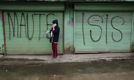 A local government worker uses a mobile phone while in front of an establishment marked with a "Maute Isis" graffiti during the clean-up drive. REUTERS/Romeo Ranoco