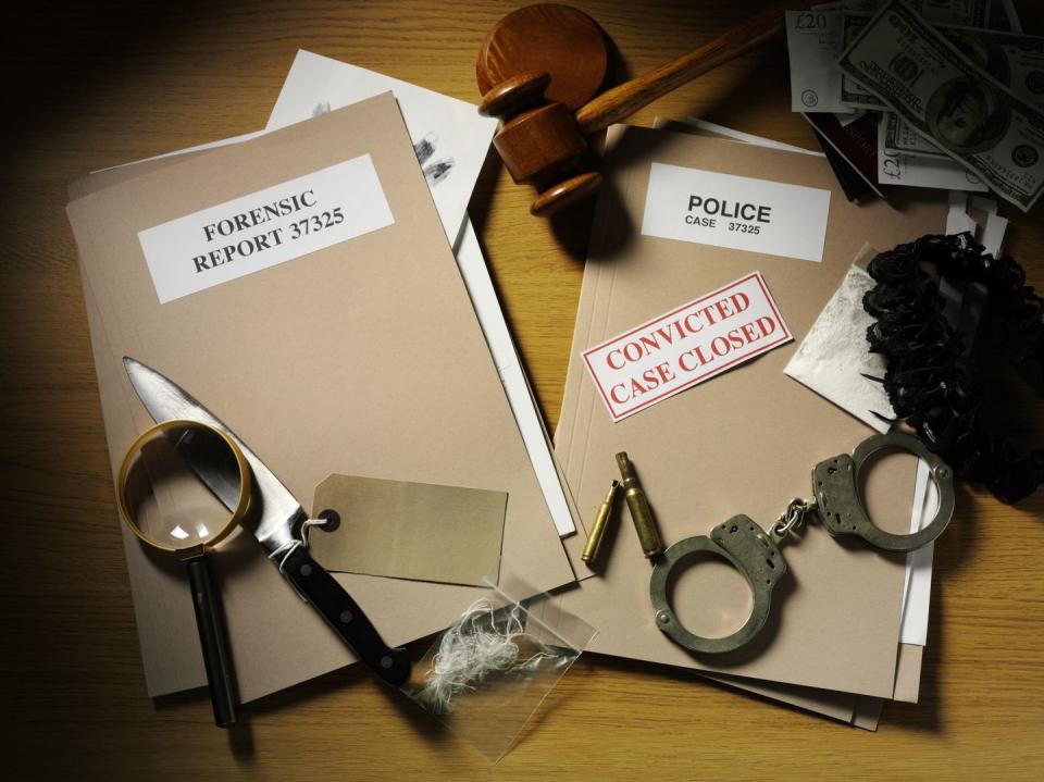 police handcuffs, knife and bullets on a desk with forensic and police paper files with a gavel and mallet, magnifying glass, currency and drugs