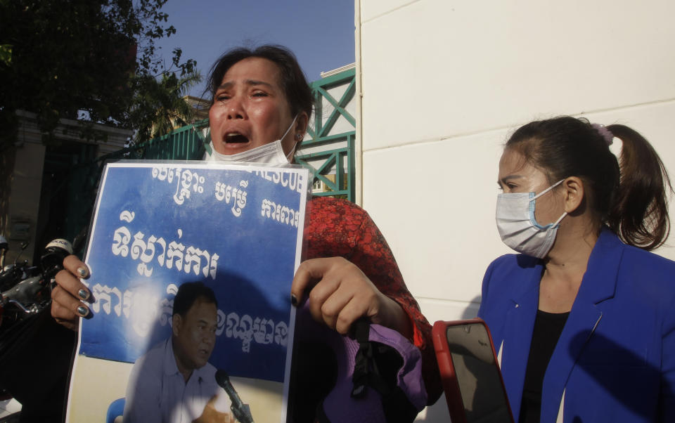 Prum Chenda, left, wife of a jailed former opposition activist, holds a portrait of her husband in front of the Phnom Penh Municipal Court, in Phnom Penh, Cambodia, Thursday, Jan. 14, 2021. The trial of more than 60 critics and opponents of the Cambodian government charged with treason and other offenses for taking part in nonviolent political activities resumed Thursday, with rights advocates skeptical that justice is being served. (AP Photo/Heng Sinith)