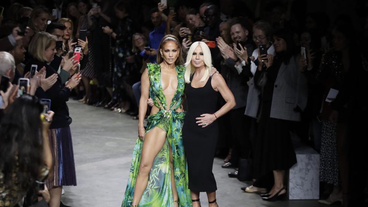 Die Schauspielerin und Tänzerin Jennifer Lopez (l) und die italienische Designerin Donatella Versace nehmen nach der Modenschau den Applaus des Publikums entgegen. Foto: Luca Bruno/AP