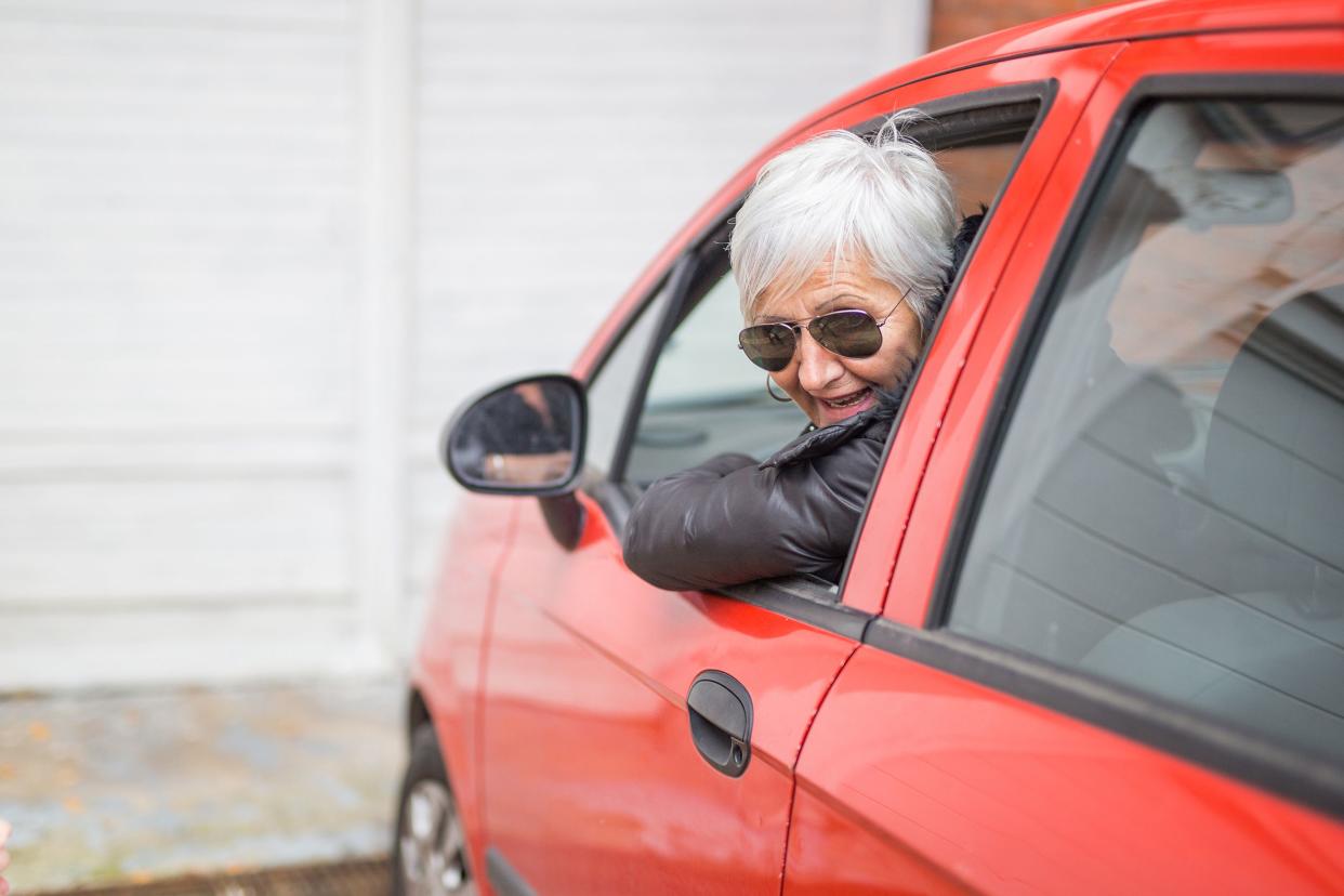 senior woman smiling in front seat of car while in driveway