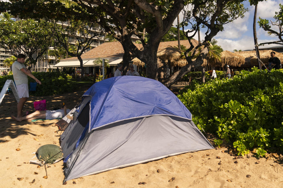 A tent sits in front of the Hula Grill Kaanapali, Wednesday, Dec. 6, 2023, at Kaanapali Beach in Lahaina, Hawaii. Residents and survivors still dealing with the aftermath of the August wildfires in Lahaina have mixed feelings as tourists begin to return to the west side of Maui, staying in hotels still housing some displaced residents. A group of survivors is camping on the resort beach to protest and raise awareness for better long-term housing options for those displaced. (AP Photo/Lindsey Wasson)