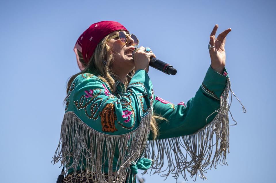 A female country singer in a fringed shirt performs onstage outdoors