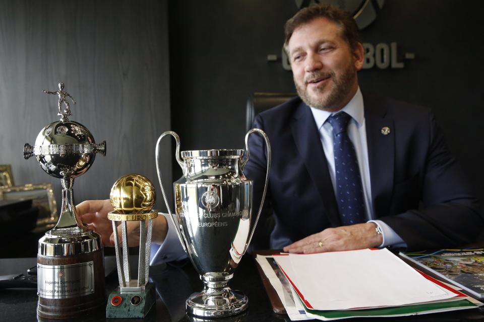 El presidente de la CONMEBOL Alejandro Domínguez toca un trofeo de la Copa Libertadores (a la izquierda) junto a los trofeos de la Liga Europa y la Liga de Campeones, durante una entrevista en la sede de la entidad en Luque, Paraguay, el miércoles 19 de febrero de 2020. (AP Foto/Jorge Saenz)