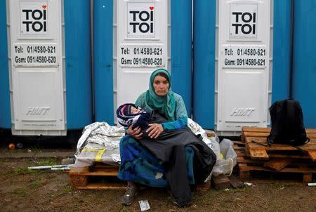 A woman carrying a child sits in front of portable toilets at a migrant camp in Opatovac, Croatia October 19, 2015. REUTERS/Dado Ruvic