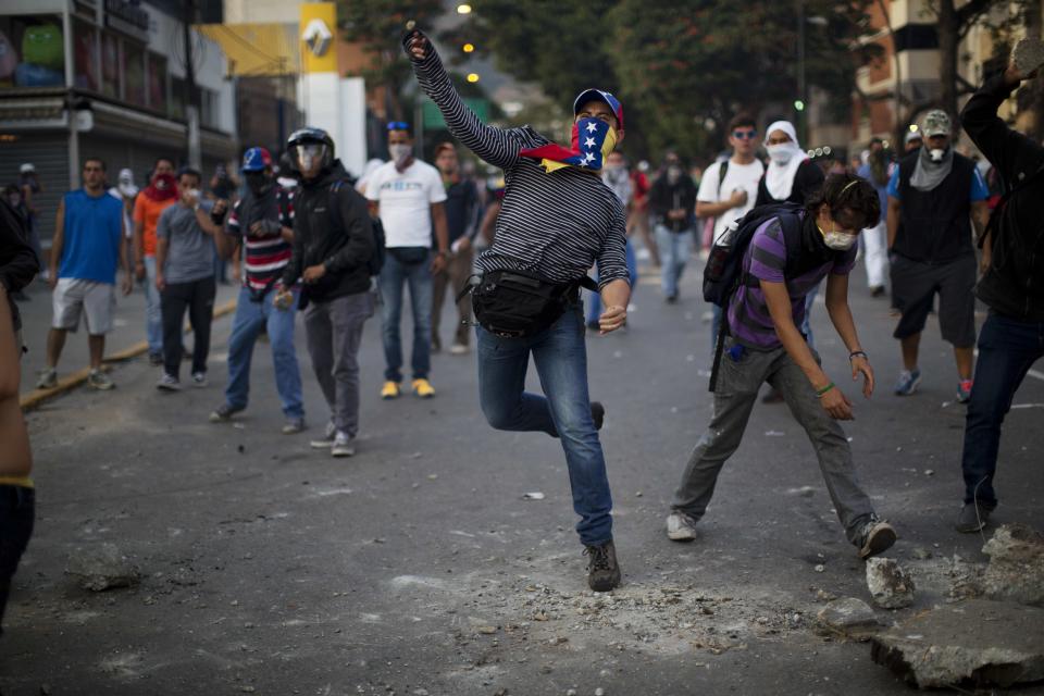 Demonstrators throw rocks to the National Bolivarian Police (BNP) during a protest in Caracas, Venezuela, Wednesday, Feb. 19, 2014. Venezuelan security forces backed by water tanks and tear gas dispersed groups of anti-government demonstrators who tried to block Caracas' main highway Wednesday evening. (AP Photo/Rodrigo Abd)