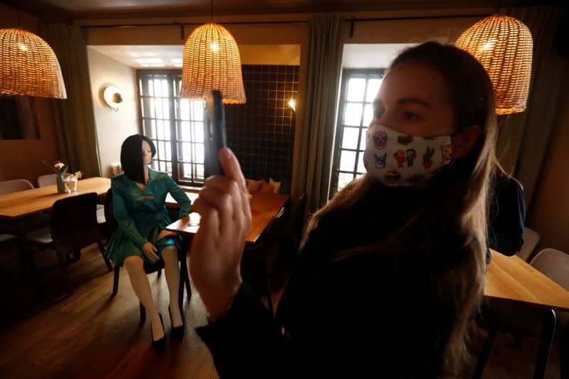 A woman wearing a protective face mask takes a picture of a mannequin inside a restaurant where mannequins dressed in creations of local designer sit at the table and bar, during the coronavirus disease (COVID-19) outbreak in Vilnius