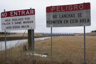 Signs in Spanish warn of approaching river side of the Rockwall-Forney Dam in Forney, Texas, Wednesday, Feb. 16, 2022. The National Inventory of Dams contains neither the hazard classification nor a condition for the dam, which impounds Lake Ray Hubbard to supply water to more than 1 million people in the Dallas area. A 2021 inspection document provided to the AP by Dallas shows the dam is classified as high hazard and has several issues. (AP Photo/LM Otero)