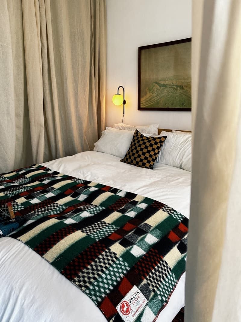 Patterned blanket on a white bed below a framed piece of artwork.