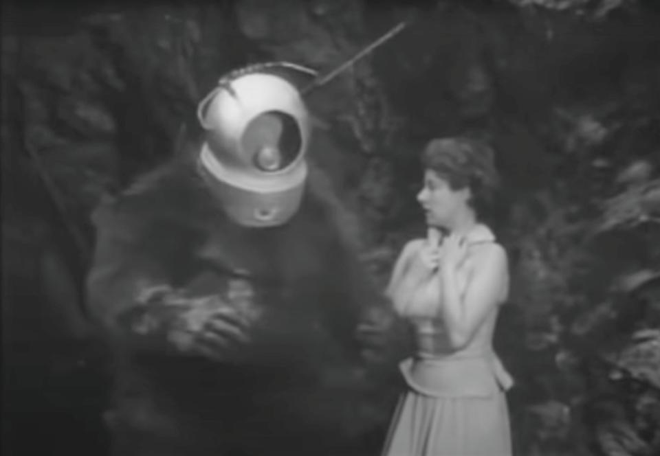 A monster with a space helmet harasses a woman