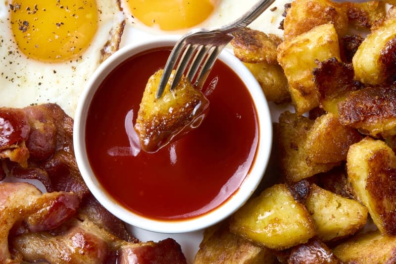 overhead shot of breakfast sauce in a small white bowl on a breakfast plate, with a potato being dipped into the sauce