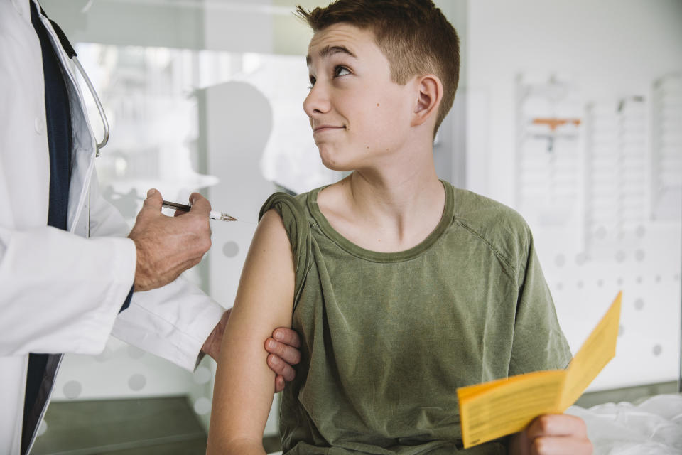 Männlicher Teenager mit Impfpass in der Hand wird geimpft
