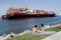 Women sunbathe on a strip of grass along Government Cut as a container ship passes by during the new coronavirus pandemic, Friday, July 3, 2020, in Miami Beach, Fla. Beaches throughout South Florida are closed for the busy Fourth of July weekend to avoid further spread of the new coronavirus. (AP Photo/Lynne Sladky)