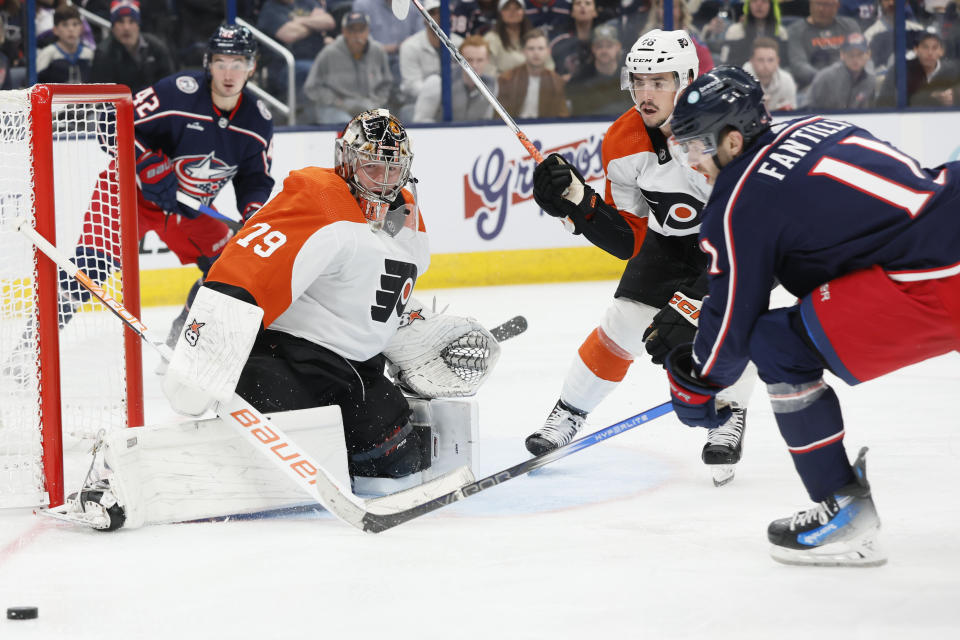 Philadelphia Flyers' Carter Hart, left, makes a save against Columbus Blue Jackets' Adam Fantilli, right, as Flyers' Morgan Frost defends during the second period of an NHL hockey game Thursday, Oct. 12, 2023, in Columbus, Ohio. (AP Photo/Jay LaPrete)