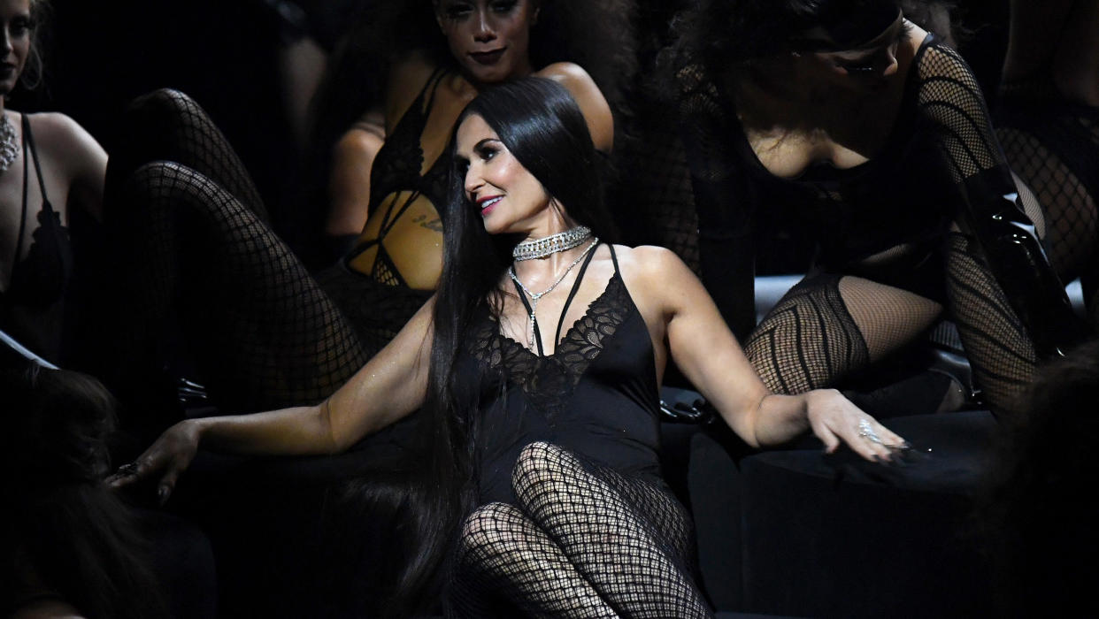 Demi Moore seated onstage, surrounded by backup dancers. (Kevin Mazur / Getty Images for Savage X Fenty )