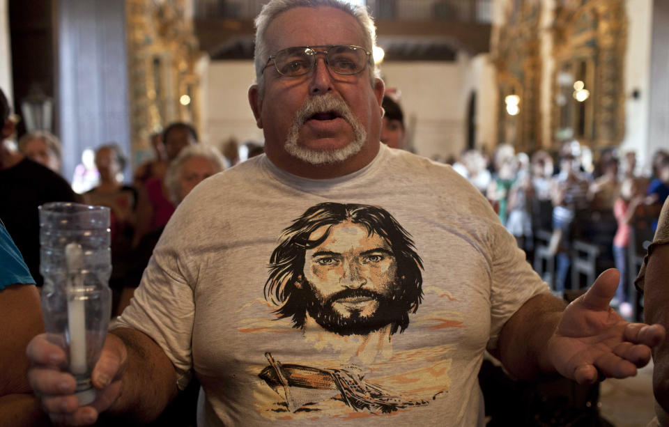 A man wearing a T-shirt decorated with the face of Jesus prays during a Mass on Good Friday at a church in Santa Maria del Rosario, Cuba, Friday, April 18, 2014. Holy Week commemorates the last week of the earthly life of Jesus Christ culminating in his crucifixion on Good Friday and his resurrection on Easter Sunday. (AP Photo/Franklin Reyes)