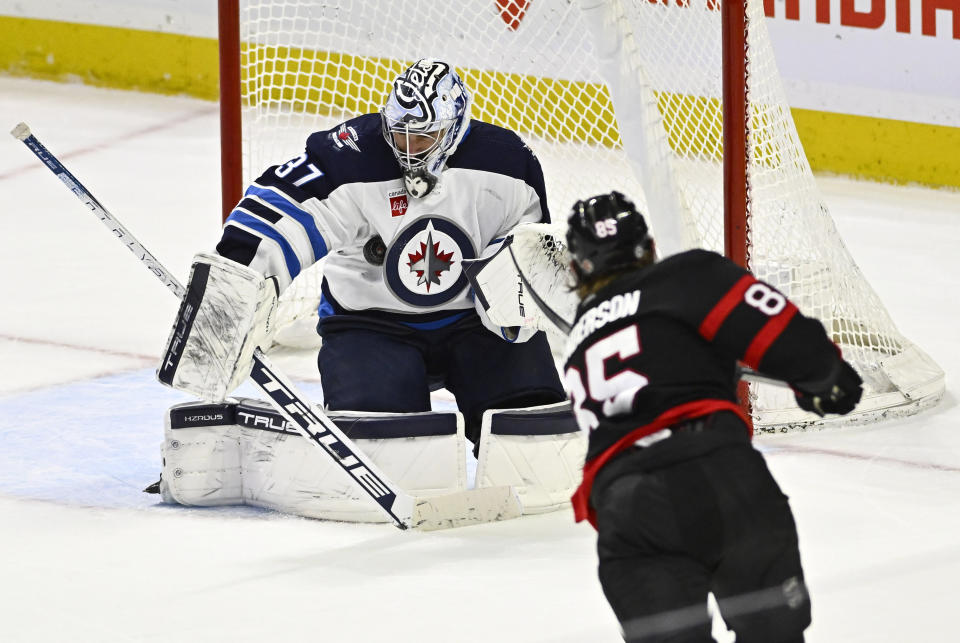 Winnipeg Jets goaltender Connor Hellebuyck (37) makes a save on a shot by Ottawa Senators defenseman Jake Sanderson (85) during overtime in an NHL hockey game, Saturday, Jan. 20, 2024, in Ottawa, Ontario. (Justin Tang/The Canadian Press via AP)