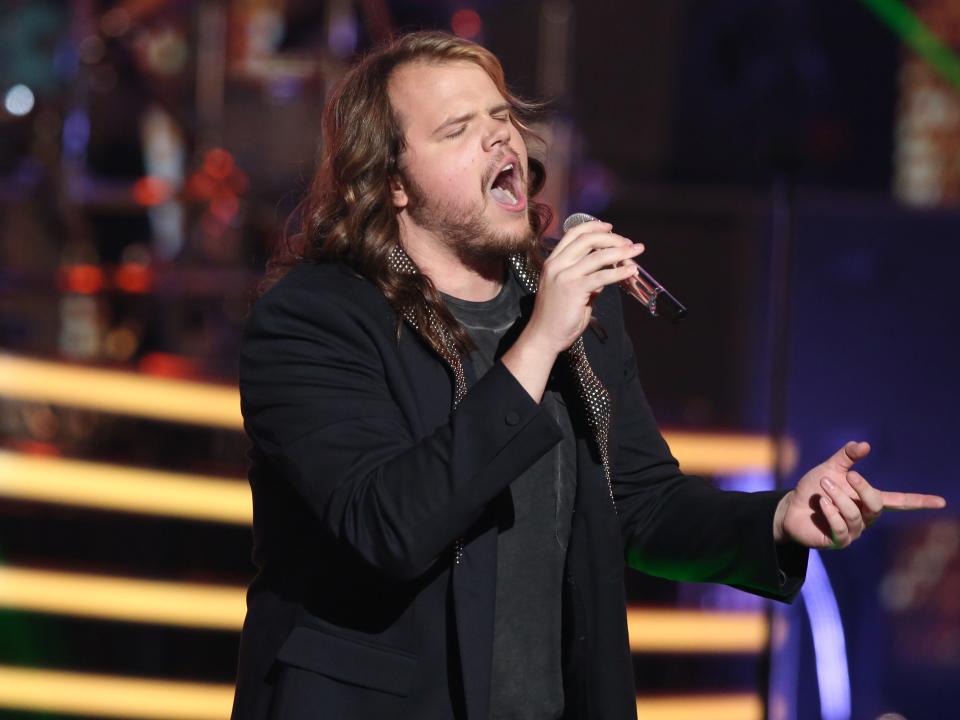 Caleb Johnson performs onstage in a black suit with yellow lights in background