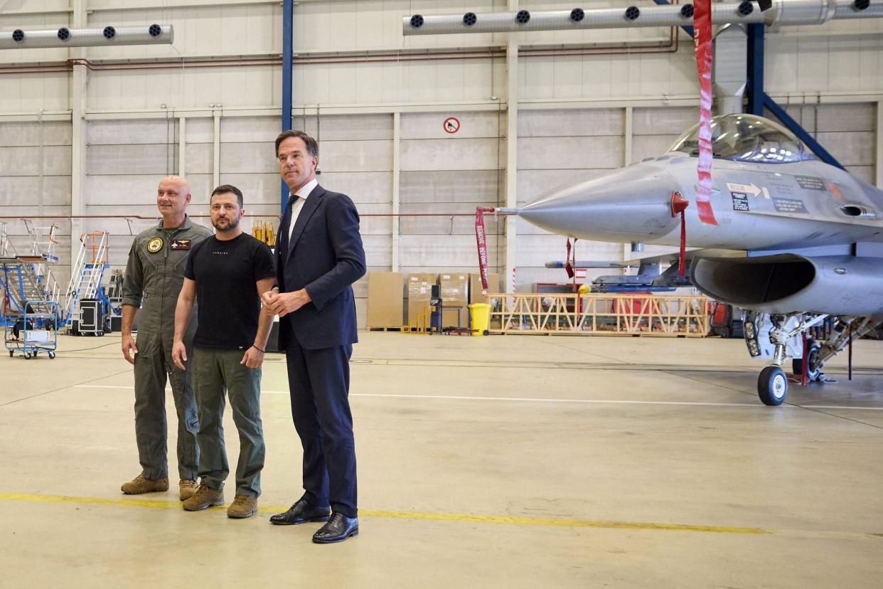 Ukraine's President Volodymyr Zelensky (C) and Dutch Prime Minister Mark Rutte (R) standing next to a F-16 fighter jet (UKRAINIAN PRESIDENTIAL PRESS SER)