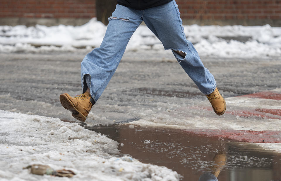 A person leaps over a puddle of water and slush as rain falls in Montreal, Friday, Dec. 23, 2022, as a storm system bears down on the region. (Graham Hughes /The Canadian Press via AP)