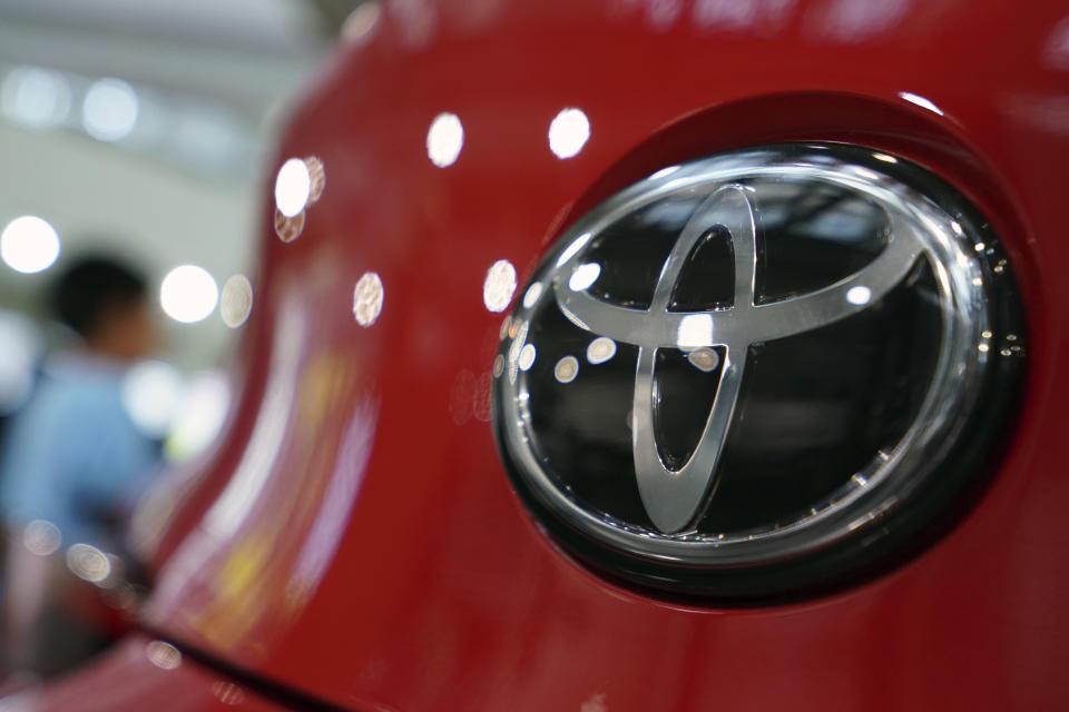 People walk by the logo of Toyota at a show room in Tokyo Friday, Aug. 2, 2019. Toyota has reported a nearly 4% increase in fiscal first quarter profit on improved sales, but the Japanese automaker slightly lowered its full year forecasts because of unfavorable currency exchange rates. (AP Photo/Eugene Hoshiko)