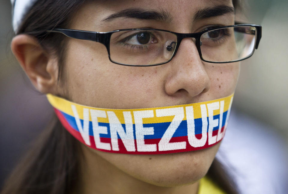 An anti-government demonstrator stands with a tri-colored ribbon covering her mouth that reads "Venezuela" during a protest in front of an office of the Organization of American States, OAS, in Caracas, Venezuela, Friday, March 21, 2014. Opposition lawmaker Maria Corina Machado is scheduled to speak before the OAS council in a closed-door session Friday in Washington D.C., presenting the situation in her country (AP Photo/Esteban Felix)