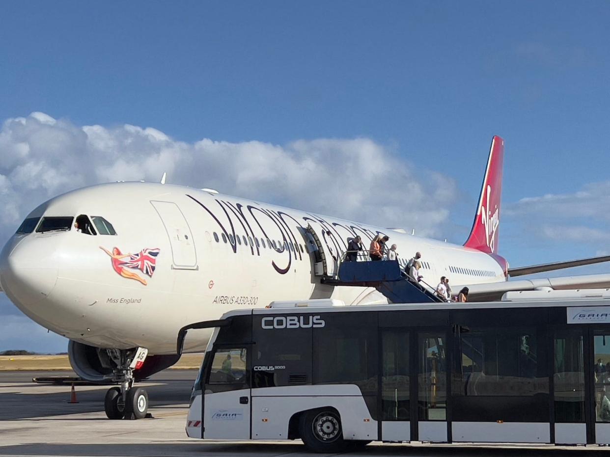 Passengers disembark a Virgin plane parked on a runway.