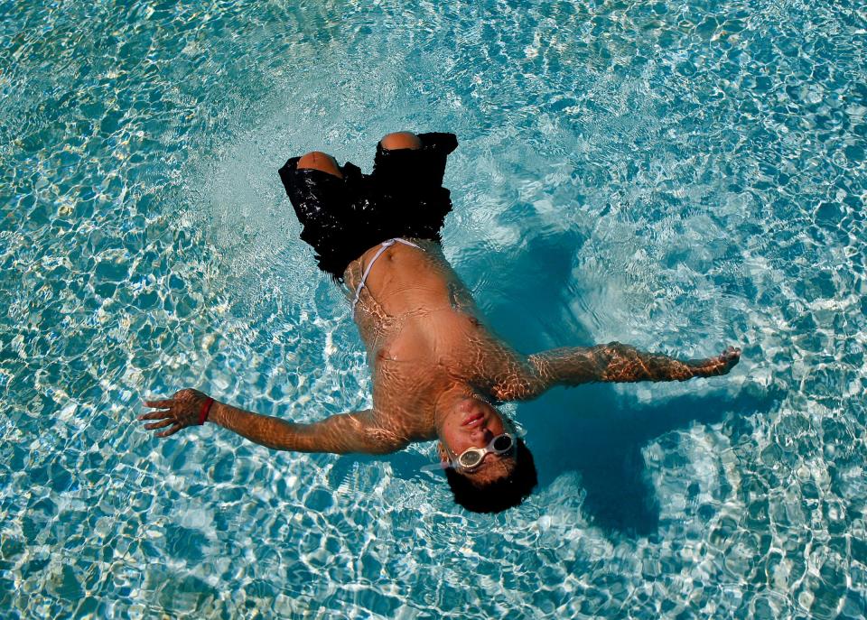 A man is floating on his back in a pool. He is wearing swim goggles and black swim trunks.