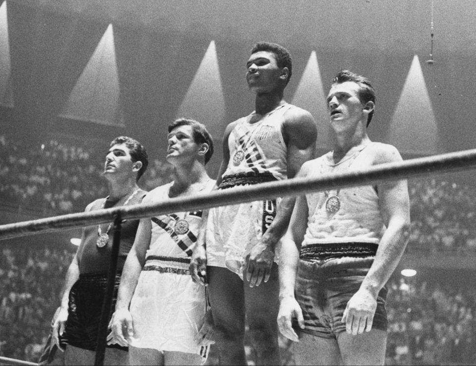 Los ganadores de las medallas olímpicas de 1960 para el boxeo de peso semipesado en el podio de los ganadores en Roma: Cassius Clay (ahora Muhammad Ali) (C), oro; Zbigniew Pietrzykowski de Polonia (R), plata; y Giulio Saraudi (Italia) y Anthony Madigan (Australia), bronce conjunto. Foto de Central Press/Getty Images)