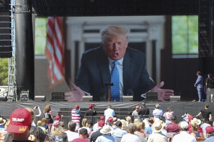 Former President Donald Trump addresses the crowd via video Saturday, June 12, 2021, at the River's Edge Apple River Concert Venue in New Richmond, Wis.  The MAGA rally was organized by pillow salesman-turned conspiracy peddler Mike Lindell.  For a few hours last weekend, thousands of Donald Trump's loyal supporters came together under the blazing sun in a field in Western Wisconsin to live in an alternate reality where the former president was still in office — or would soon return.  (AP Photo/Jill Colvin)