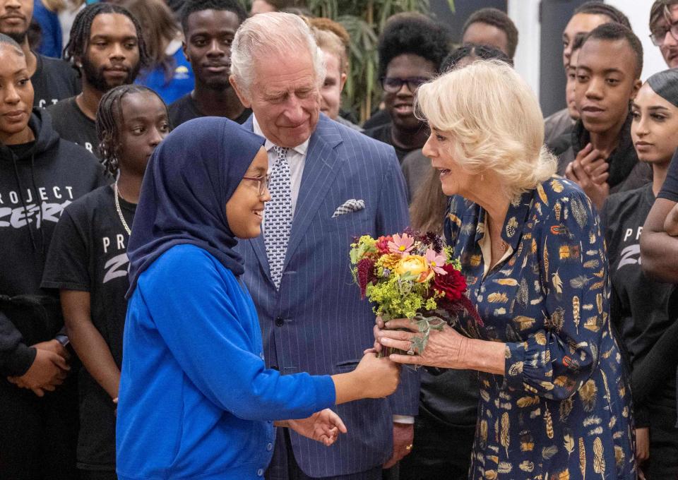 Queen Consort Camilla, flanked by King Charles III, received a flower bouquet as she arrives to meet with members and staff of "Project Zero," dedicated to engaging young people in positive activities and promoting community cohesion, during the royal couple's visit to Walthamstow in east London, on Oct. 18, 2022.