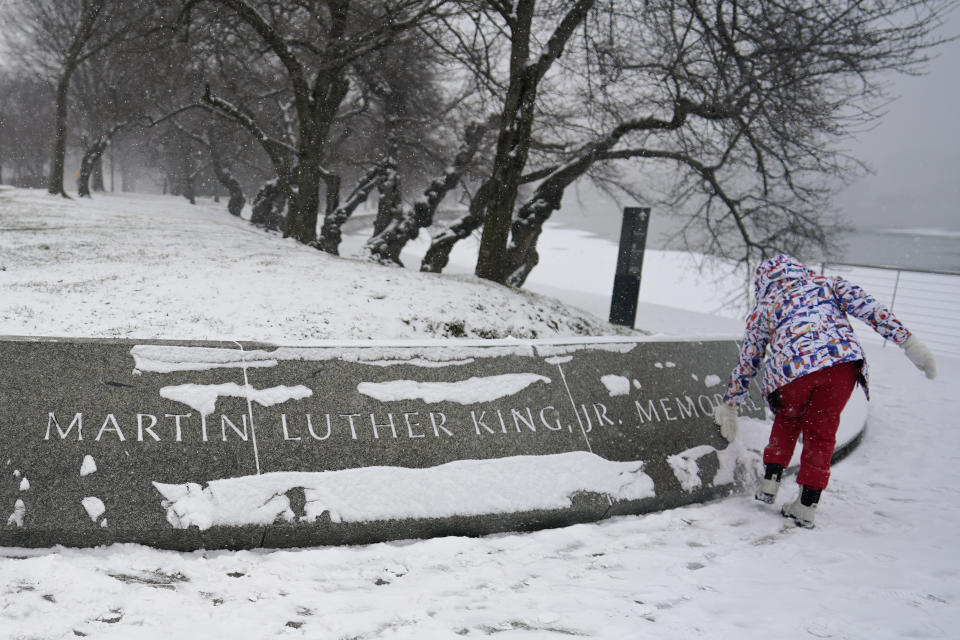 Shelby Batch, 12, of California, clears snow from the Martin Luther King, Jr. Memorial in Washington, Sunday, Jan. 16, 2022. Ceremonies scheduled for the site on Monday, to mark the Martin Luther King, Jr. national holiday, have been canceled because of the weather. (AP Photo/Carolyn Kaster)