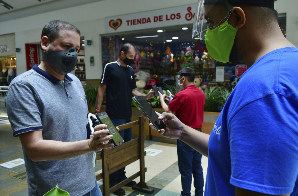 Empleado del centro comercial El Tesoro de Medellín usan teléfonos para escanear una aplicación de los teléfonos de los visitantes para asegurarse de que están autorizados a salir de sus casas durante la pandemia del corinavirus, en foto del 8 de junio del 2020. (AP Photo/Luis Benavides)